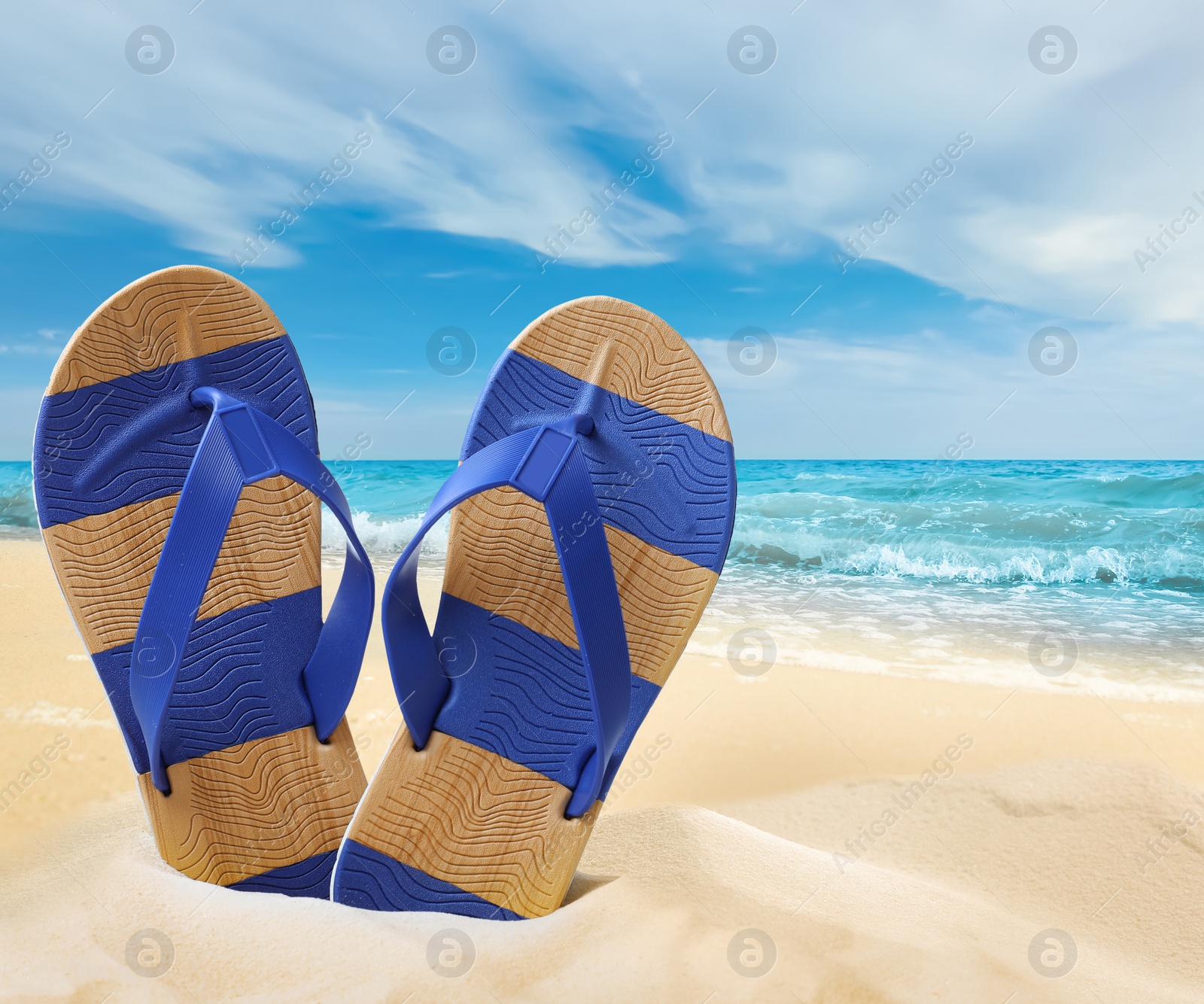 Image of Striped flip flops on sandy beach near sea