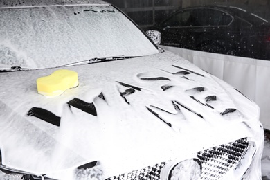 Photo of Inscription WASH ME and sponge on automobile covered with foam at car wash