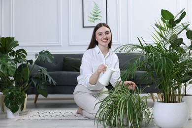 Photo of Beautiful young woman watering green potted houseplants at home