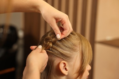 Photo of Professional hairdresser braiding girl's hair in beauty salon, closeup