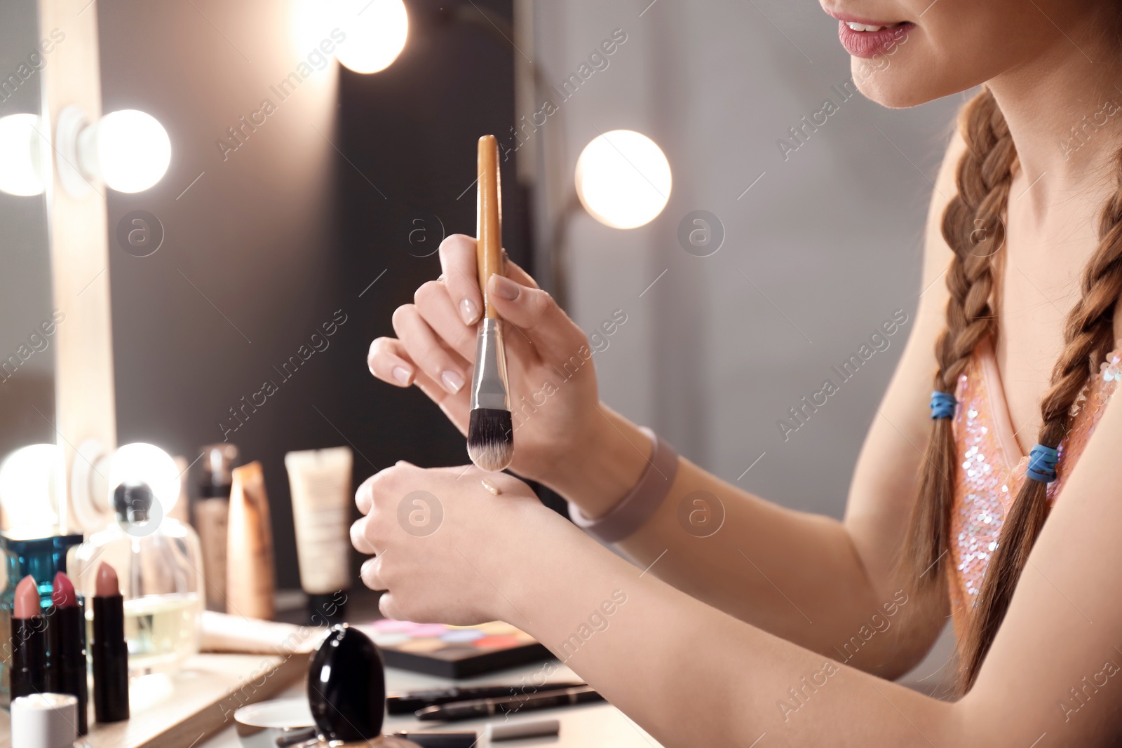 Photo of Young woman applying foundation on her hand in makeup room, closeup