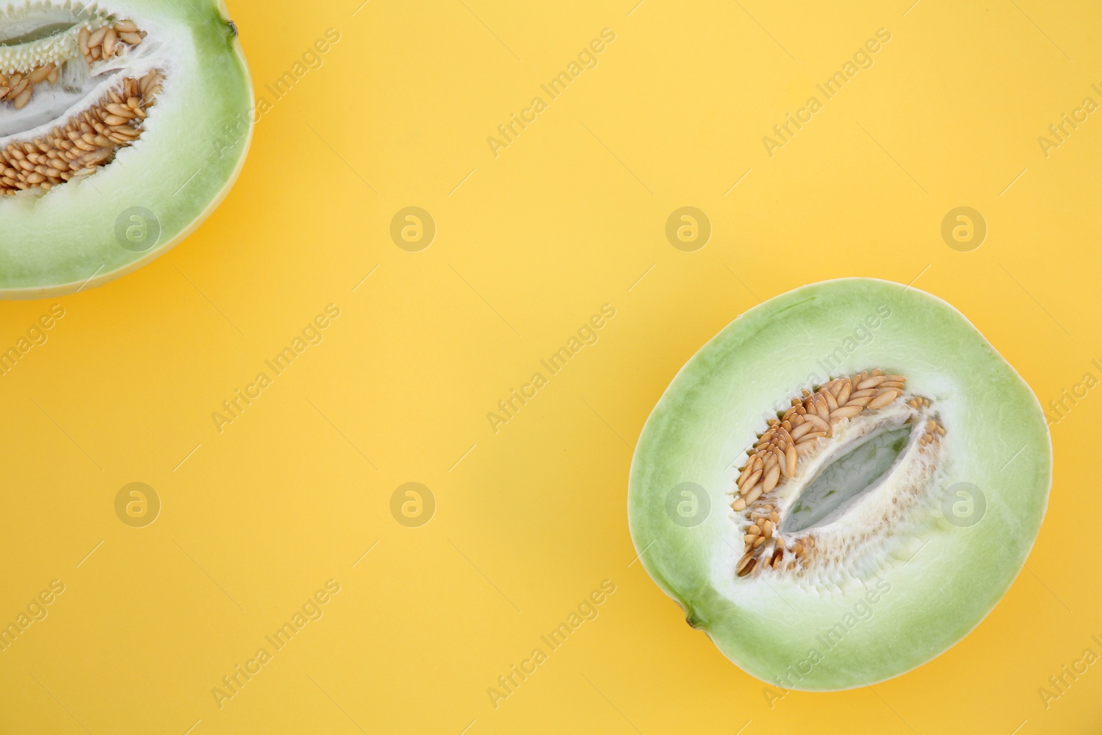Photo of Halves of fresh ripe honeydew melon on yellow background, flat lay. Space for text