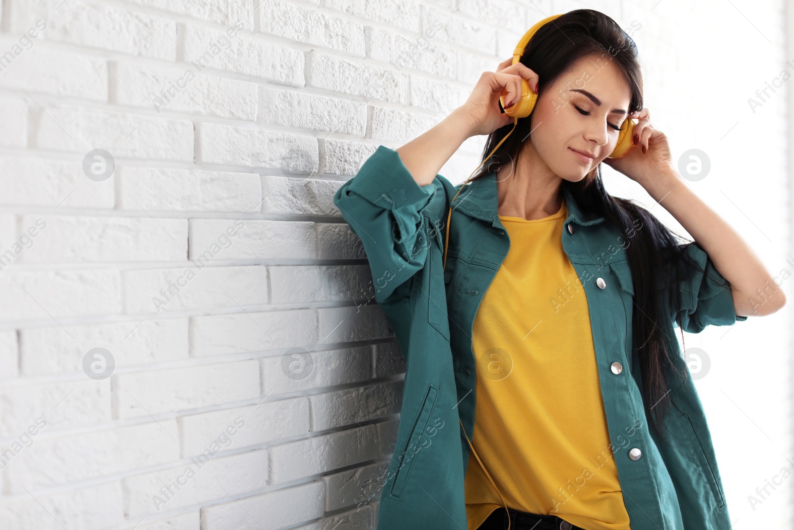 Photo of Portrait of beautiful woman listening to music with headphones near brick wall. Space for text