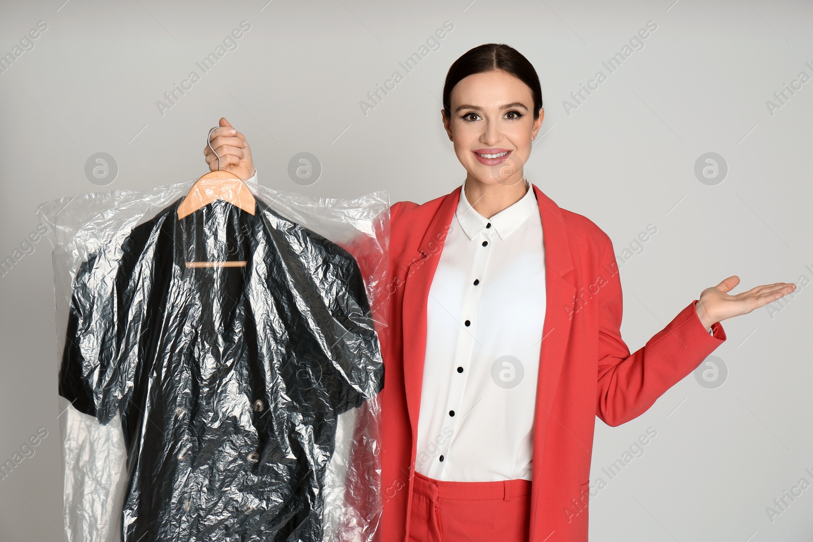 Photo of Young woman holding hanger with dress on light grey background. Dry-cleaning service