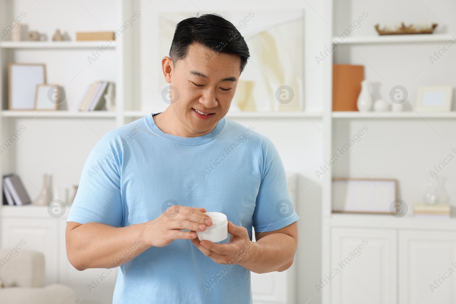 Photo of Handsome man with jar of body cream at home. Space for text