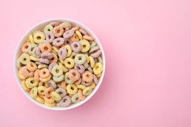 Photo of Tasty cereal rings in bowl on pink table, top view. Space for text