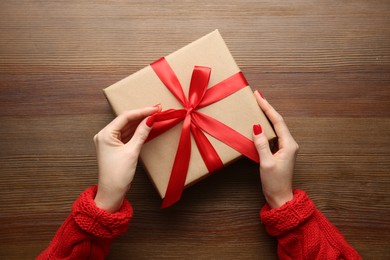 Photo of Woman holding Christmas gift box at wooden table, top view