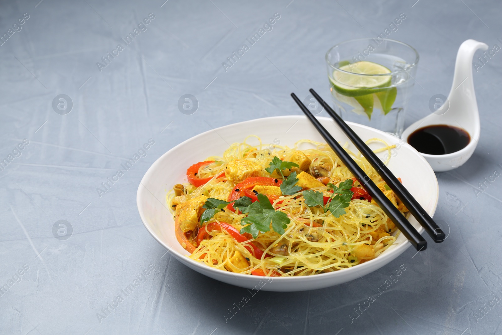 Photo of Stir-fry. Delicious cooked noodles with chicken and vegetables in bowl served on gray textured table, space for text