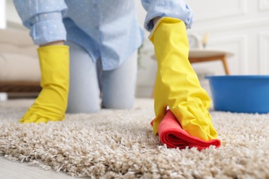 Woman in rubber gloves cleaning carpet with rag indoors, closeup. Space for text