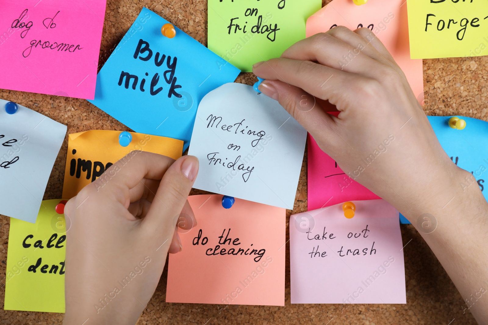 Photo of Woman pinning paper note with phrase Meeting On Friday to cork board, closeup