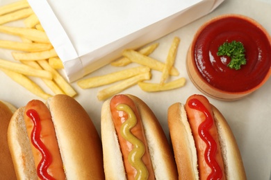 Photo of Composition with hot dogs, french fries and sauce on parchment paper, top view