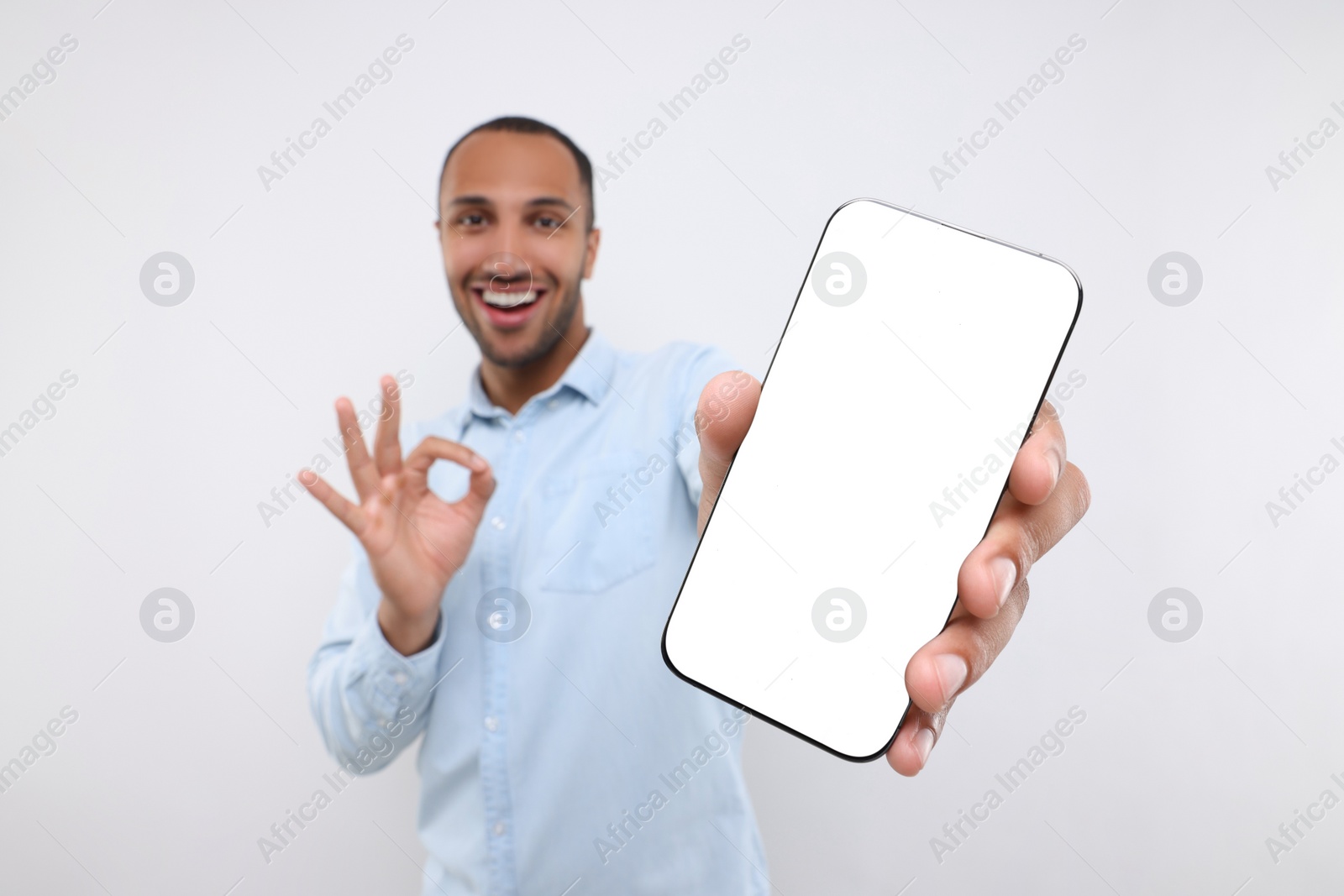 Photo of Young man showing smartphone in hand and OK gesture on white background, selective focus. Mockup for design