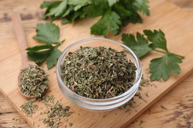 Bowl and spoon with dried parsley on wooden table, closeup