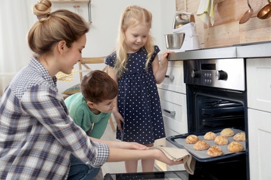 Photo of Mother and her children taking out cookies from oven in kitchen