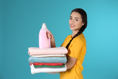 Happy young woman holding clean clothes and laundry detergent on color background