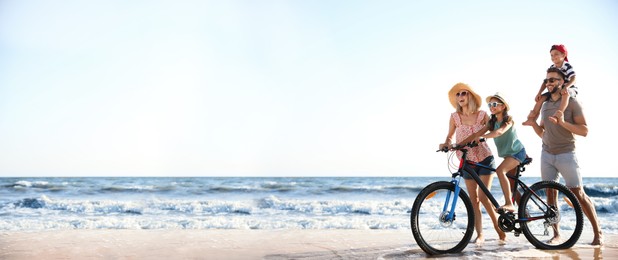 Image of Happy family with bicycle on sandy beach near sea, space for text. Banner design