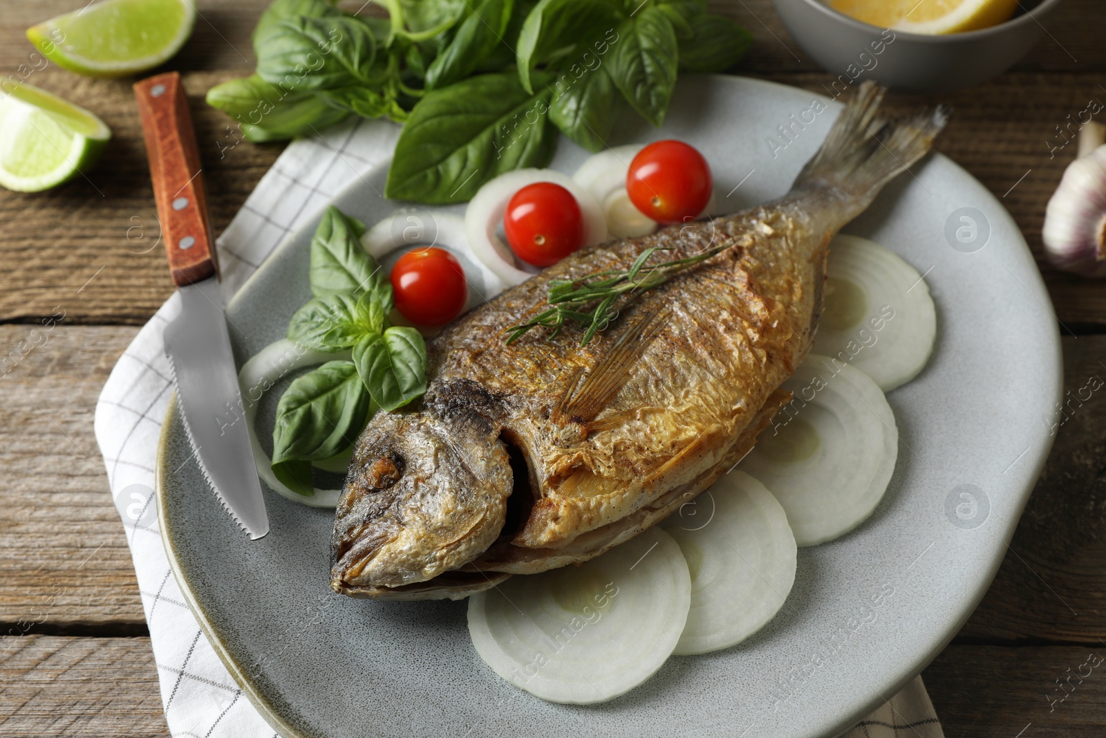 Photo of Delicious dorado fish with vegetables and herbs served on wooden table