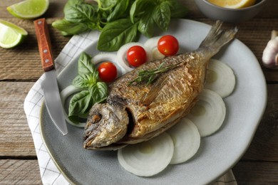 Photo of Delicious dorado fish with vegetables and herbs served on wooden table