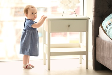 Photo of Cute baby holding on to table in bedroom. Learning to walk