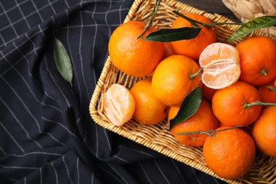 Photo of Fresh ripe tangerines with green leaves in wicker basket on table, top view