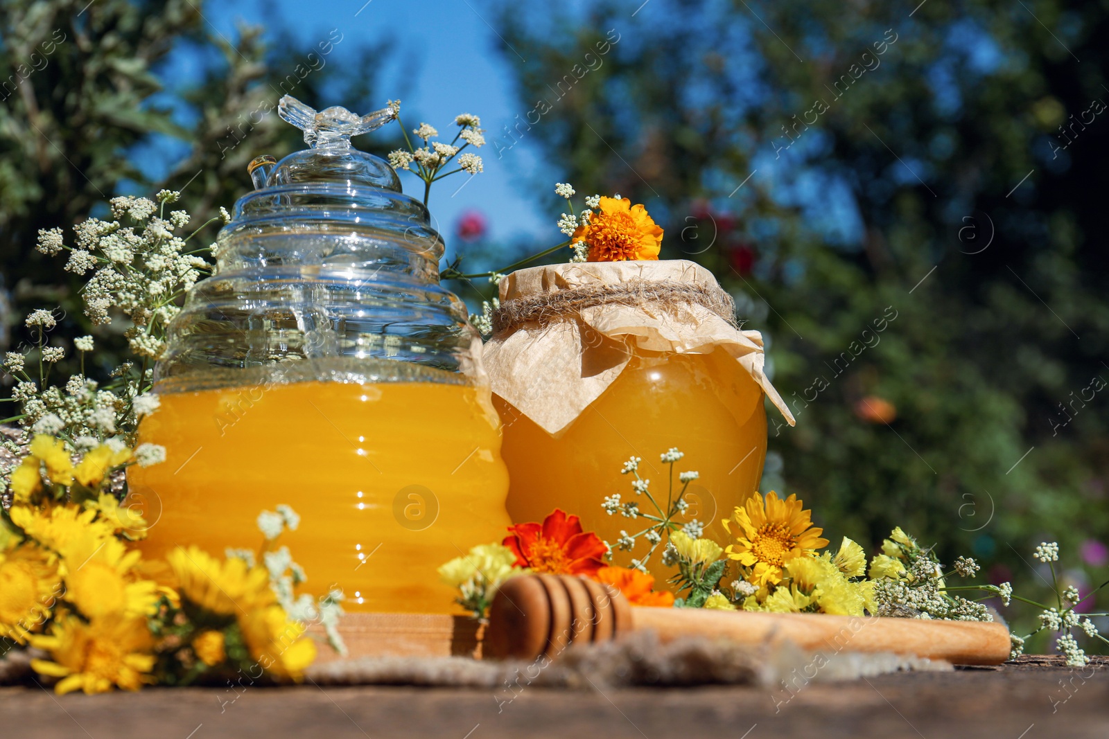 Photo of Delicious fresh honey and beautiful flowers on wooden table in garden