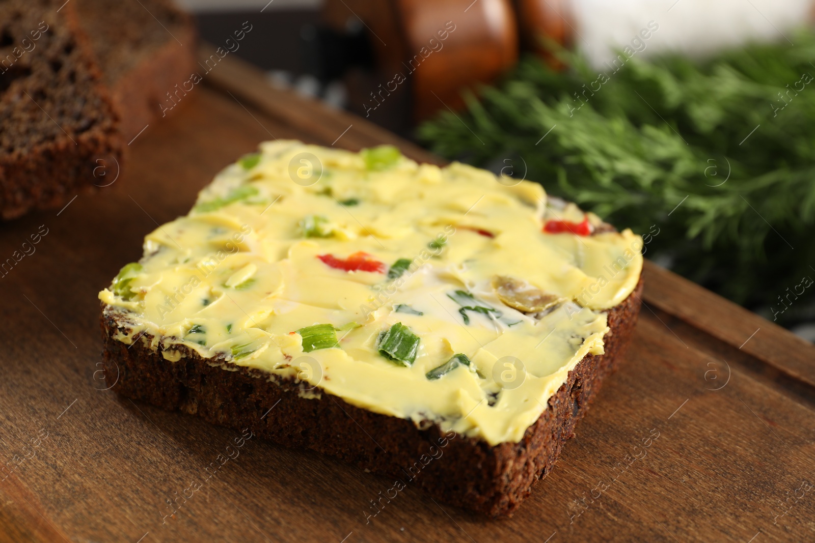 Photo of Tasty butter with green onion, chili pepper and rye bread on wooden board, closeup