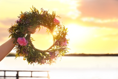 Young woman holding wreath made of beautiful flowers near river, closeup