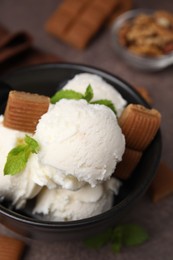 Photo of Tasty ice cream with caramel candies and mint in bowl on brown table, closeup
