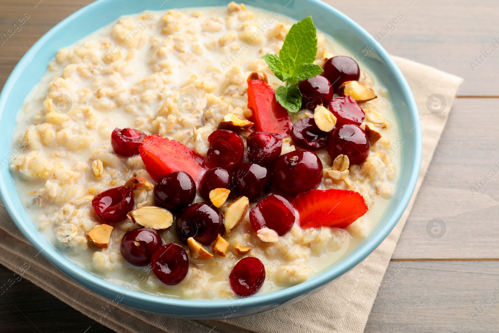 Photo of Bowl of oatmeal porridge served with berries on wooden table, closeup