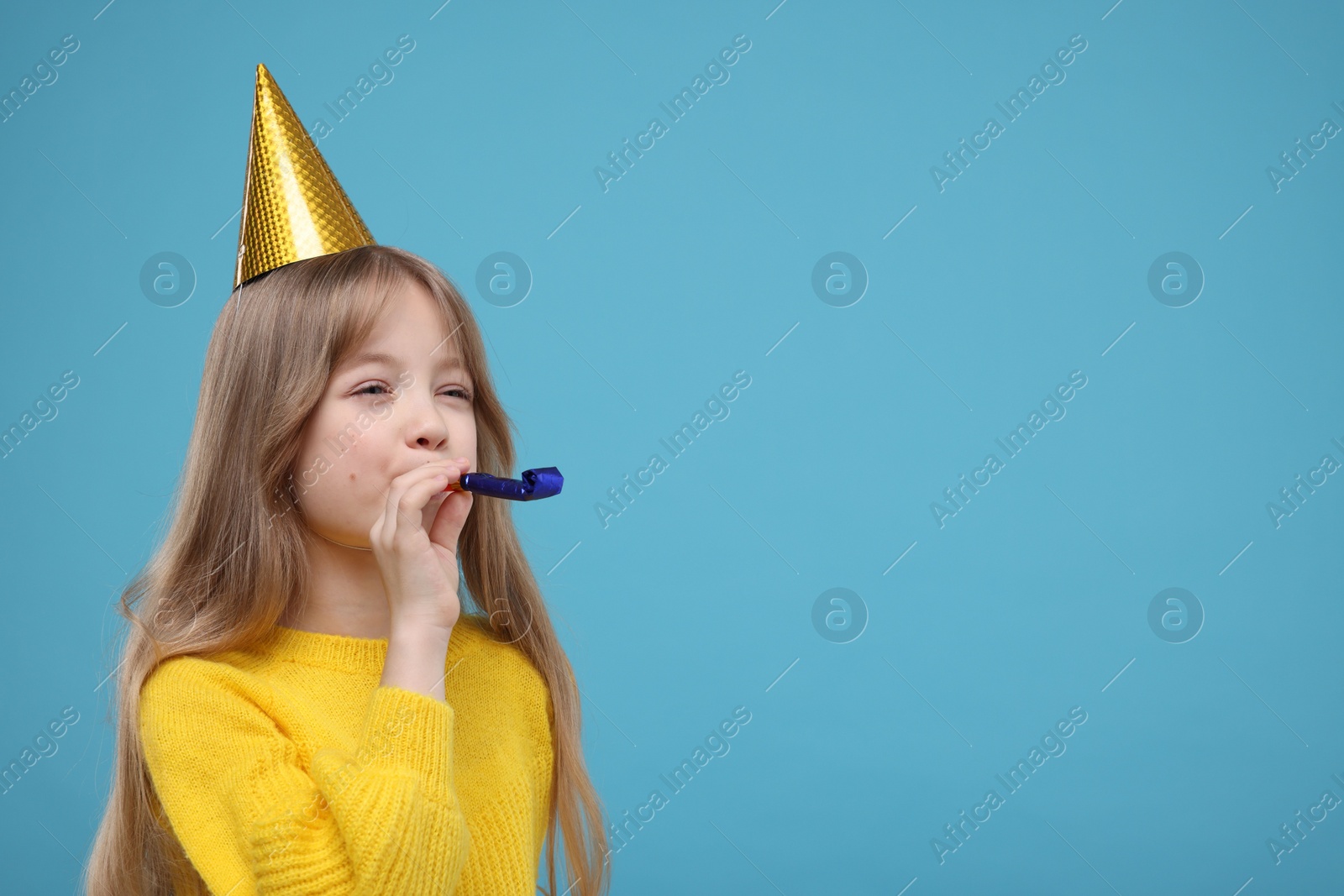 Photo of Cute little girl in party hat with blower on light blue background. Space for text