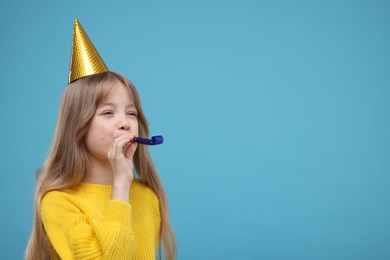 Cute little girl in party hat with blower on light blue background. Space for text