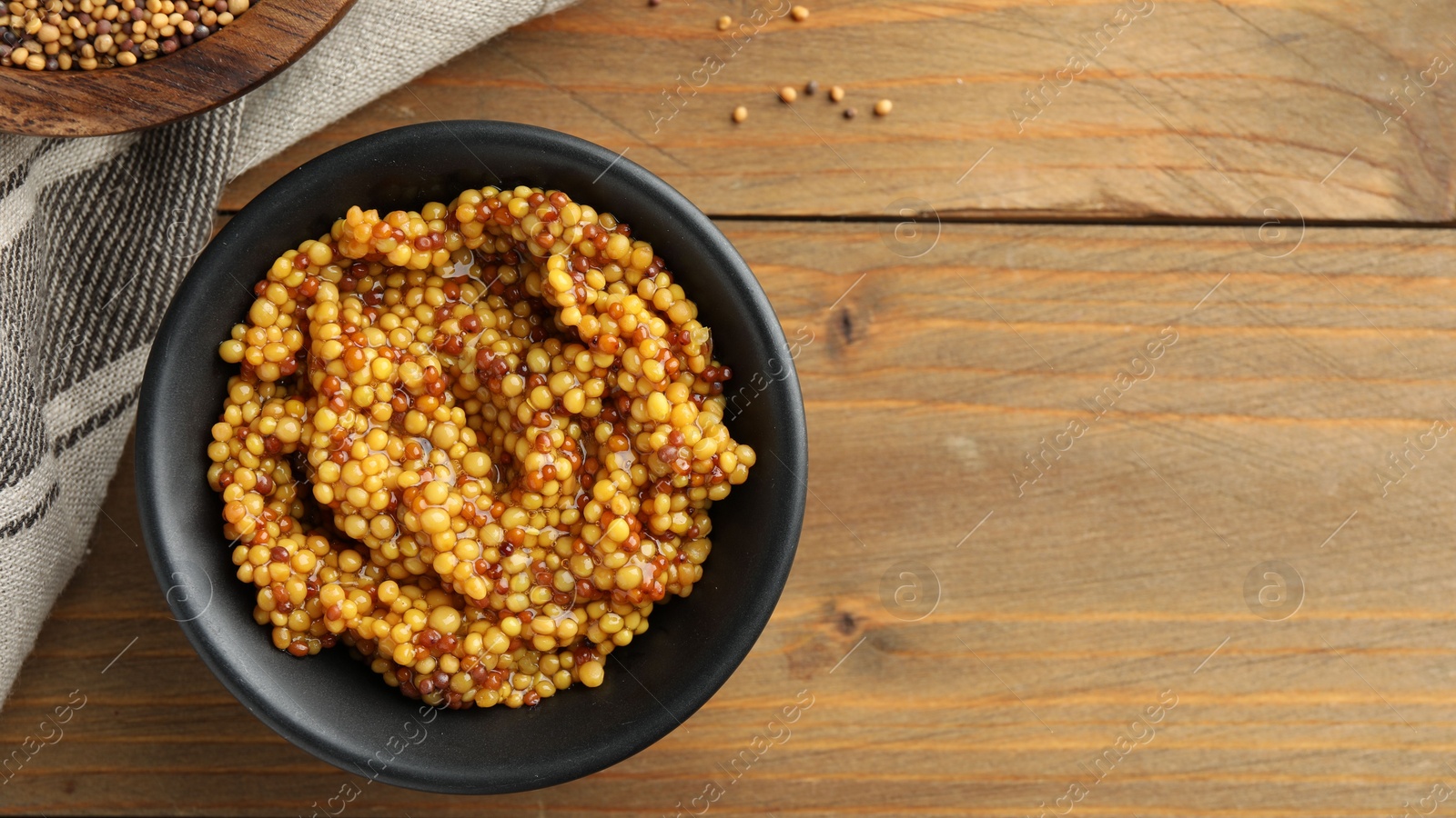 Photo of Fresh whole grain mustard in bowl on wooden table, top view. Space for text