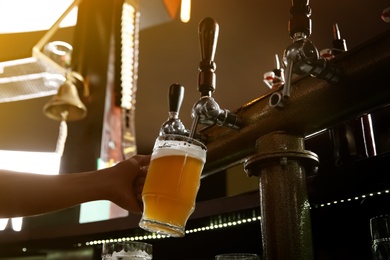 Photo of Bartender pouring beer from tap into glass in bar
