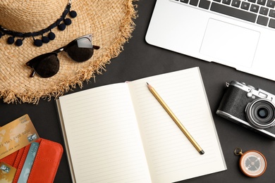 Flat lay composition with tourist items and notebook on black background, space for text. Travel agency