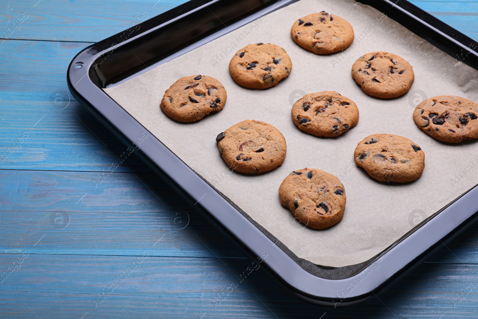 Photo of Baking pan with parchment paper and tasty cookies on light blue wooden table