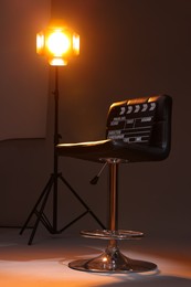 Casting call. Chair, clapperboard and lamp in modern studio, low angle view