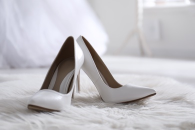 Photo of White wedding shoes on furry rug in room