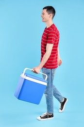 Man with cool box walking on light blue background