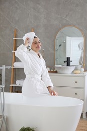 Beautiful young woman sitting on edge of tub in bathroom