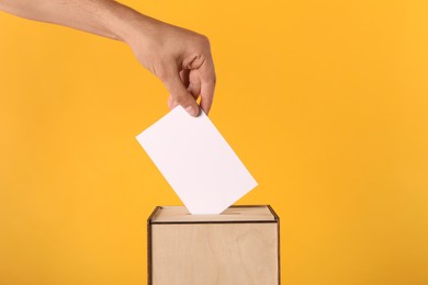 Photo of Man putting his vote into ballot box on yellow background, closeup