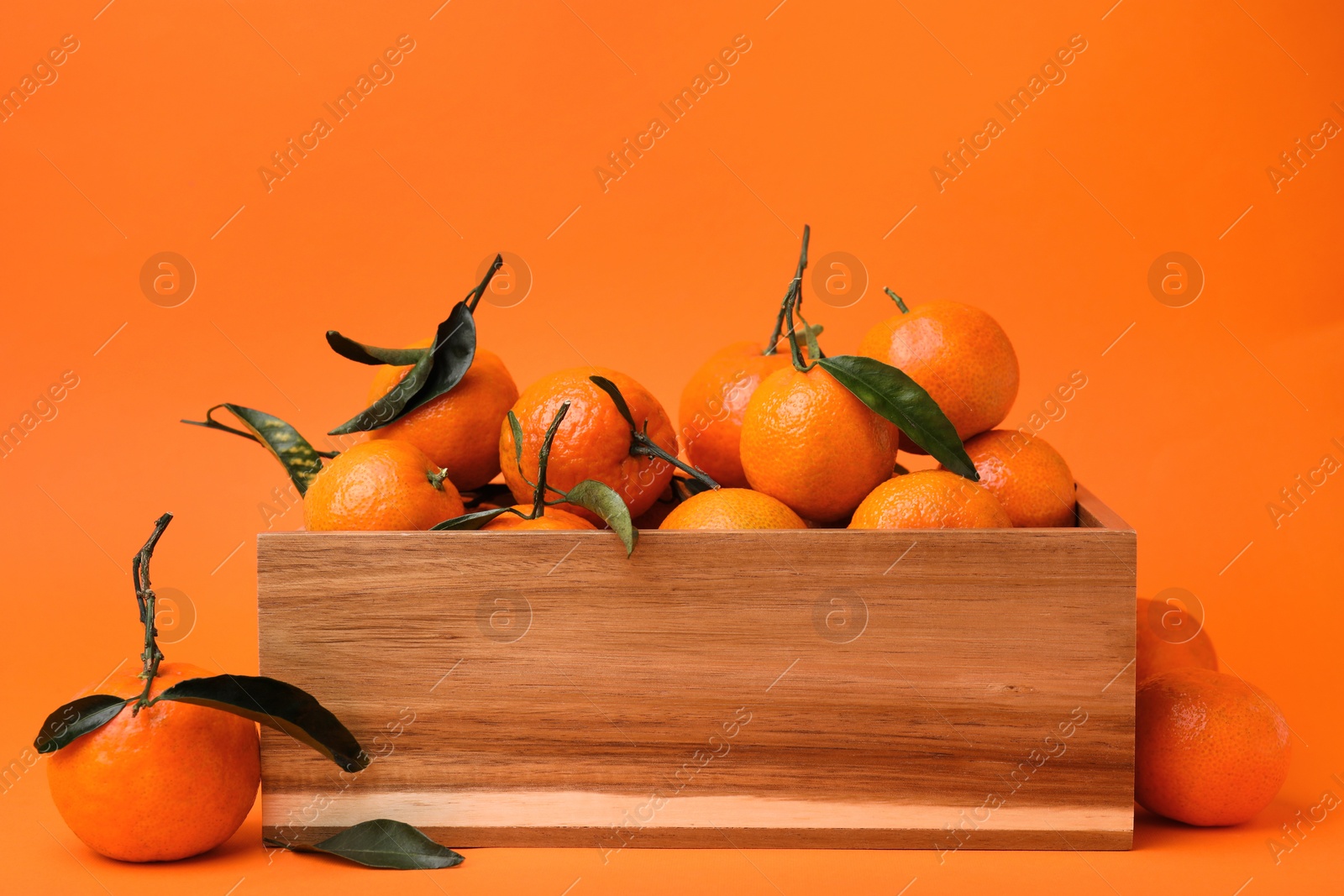 Photo of Wooden crate with fresh ripe tangerines and leaves on orange table
