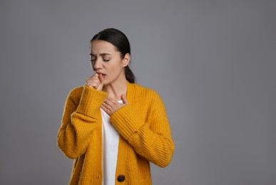 Photo of Young woman coughing on grey background, space for text. Cold symptoms