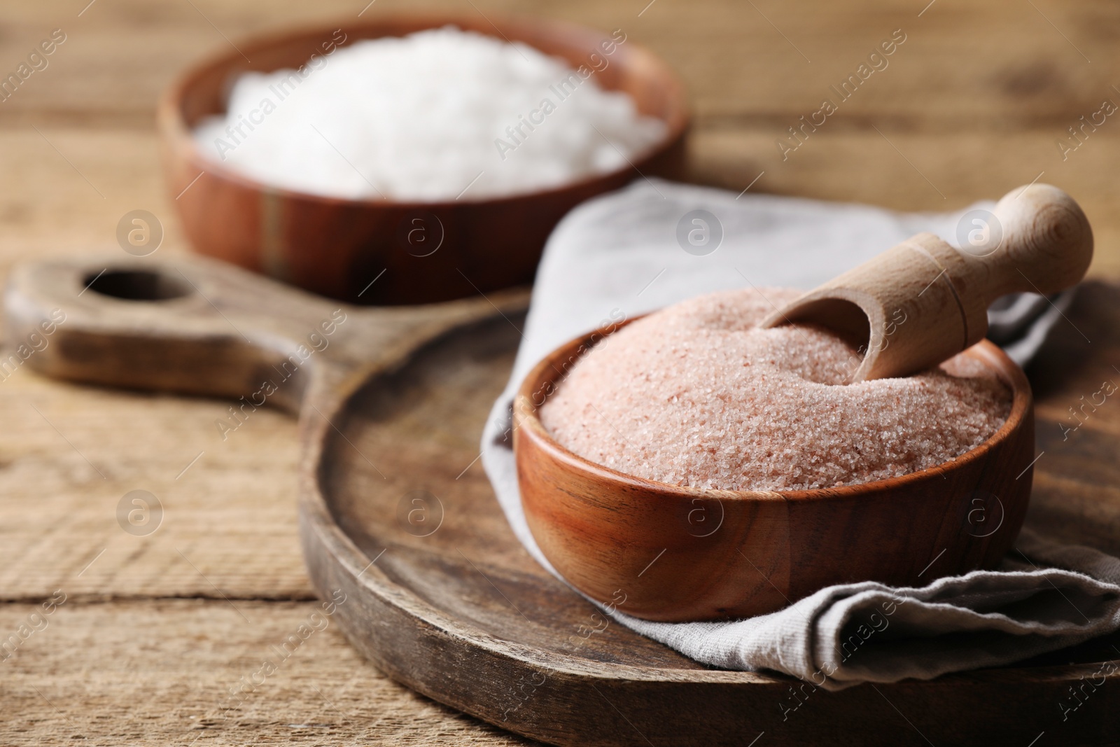 Photo of Different salt and scoop in bowl on wooden table, closeup. Space for text