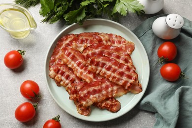 Photo of Fried bacon slices, tomato, parsley, oil and spices on grey textured table, flat lay