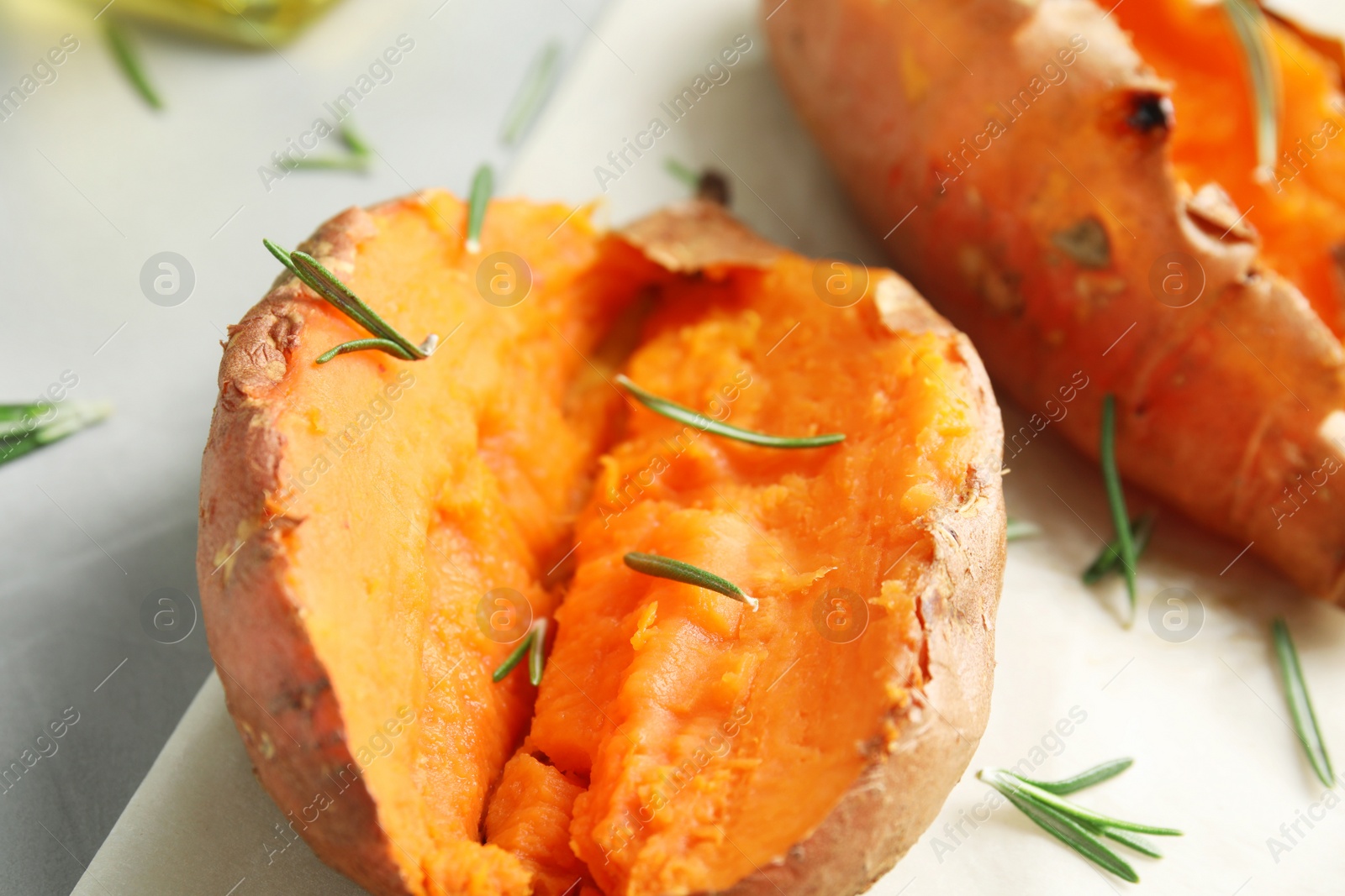 Photo of Delicious baked sweet potatoes with rosemary on parchment, closeup