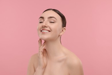 Smiling woman touching her neck on pink background