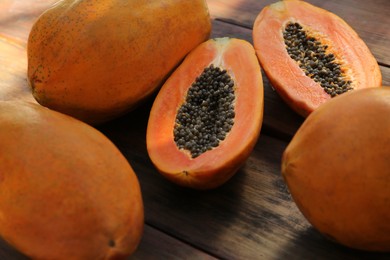 Photo of Fresh ripe cut and whole papaya fruits on wooden table, closeup