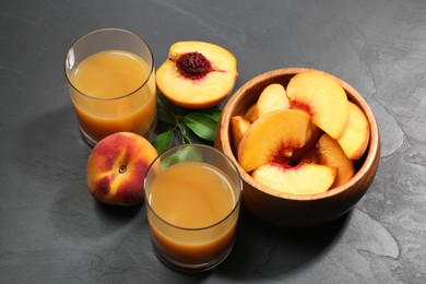 Photo of Glasses of delicious peach juice, fresh fruits and leaves on black table