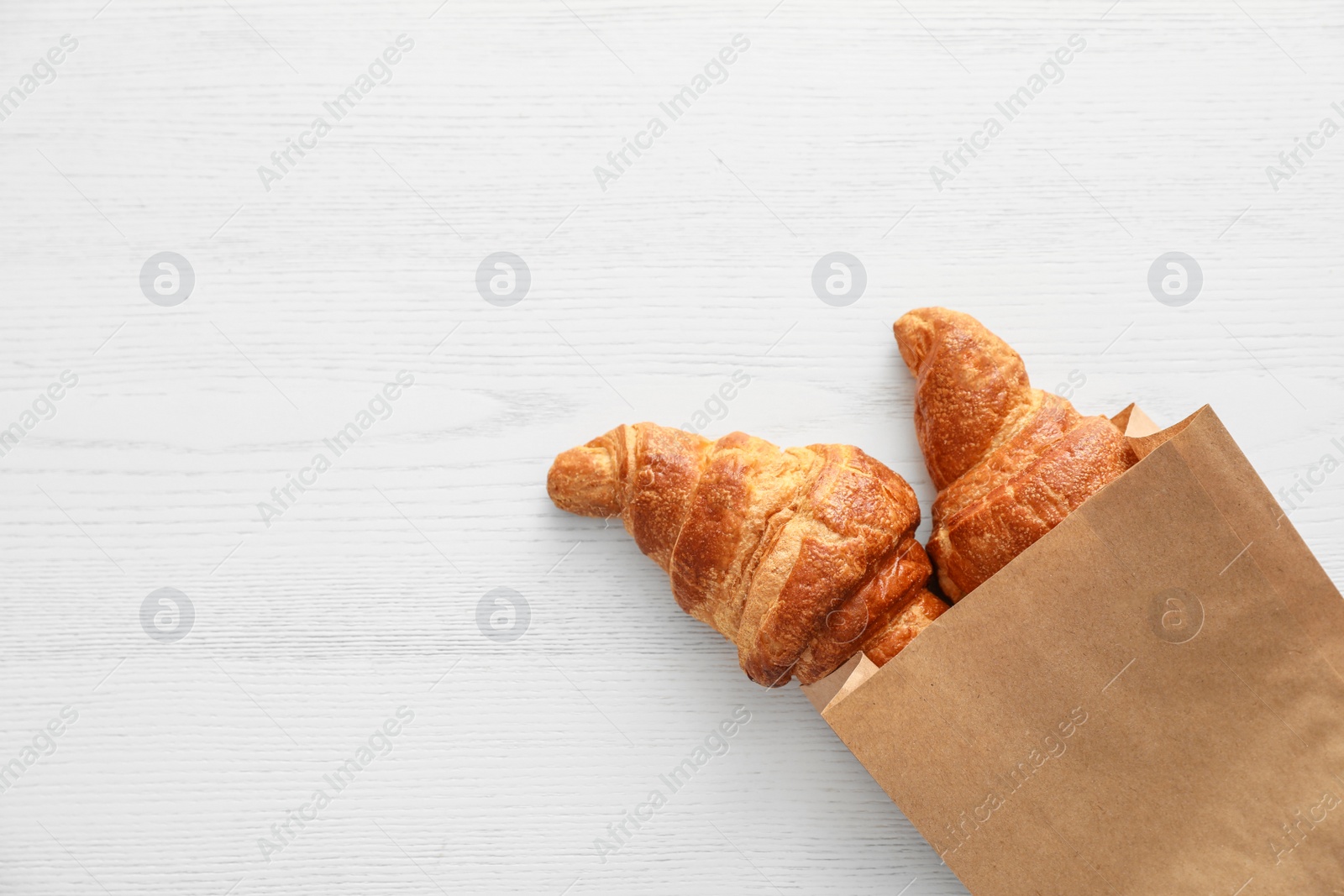 Photo of Paper bag with pastry on light wooden background, top view with space for text