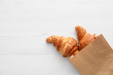 Paper bag with pastry on light wooden background, top view with space for text